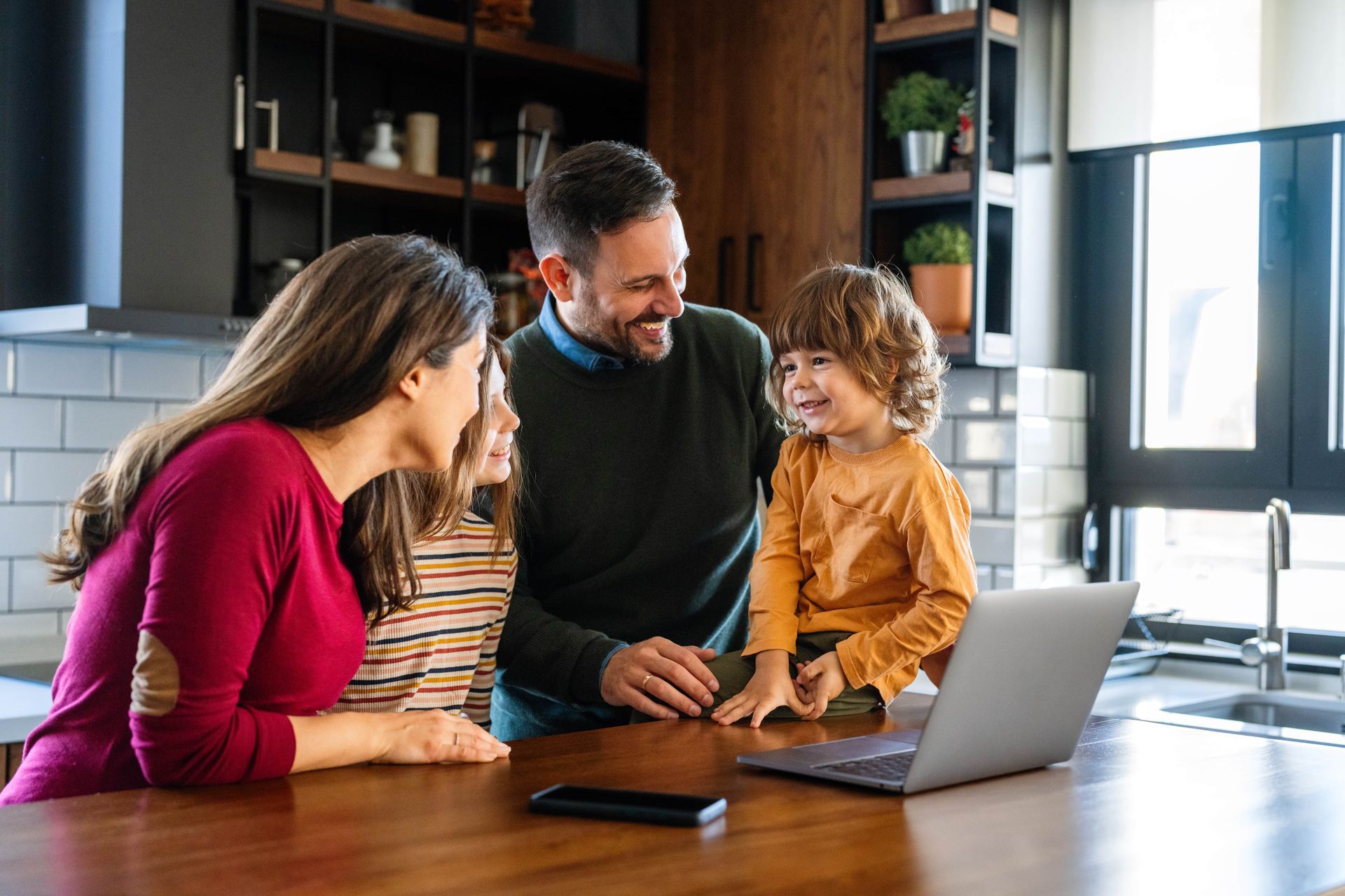 A family is sitting at a table in front of a laptop computer.