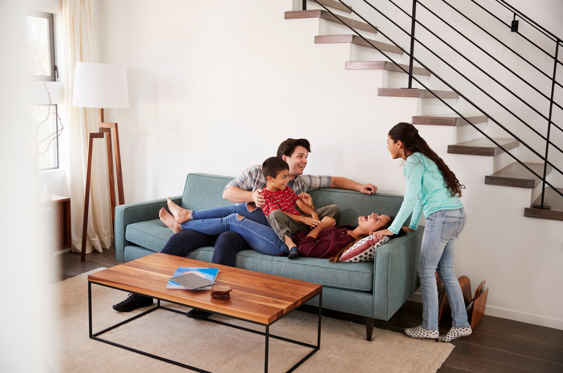 A family is sitting on a couch in a living room next to stairs.