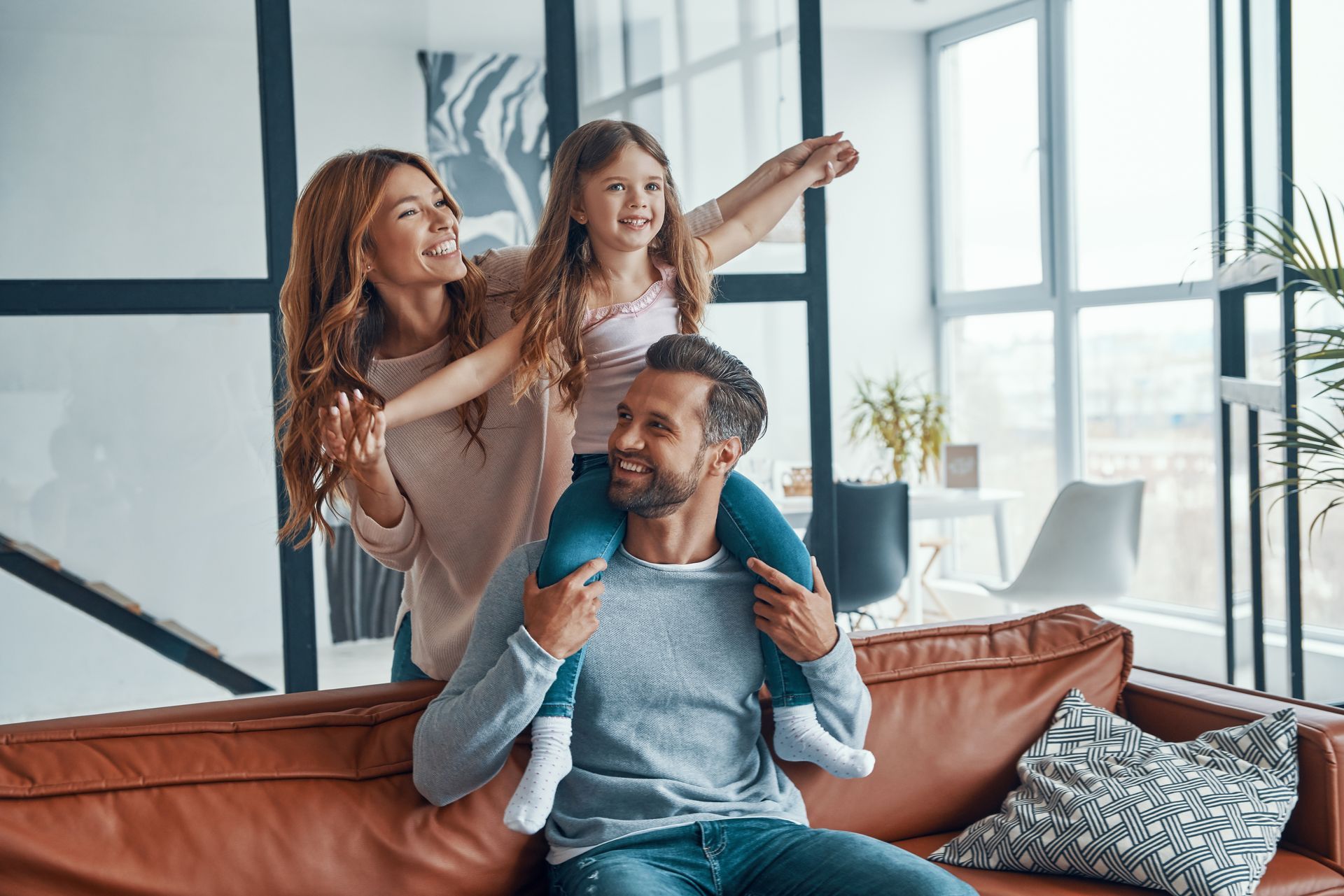 A man is sitting on a couch holding a little girl on his shoulders.