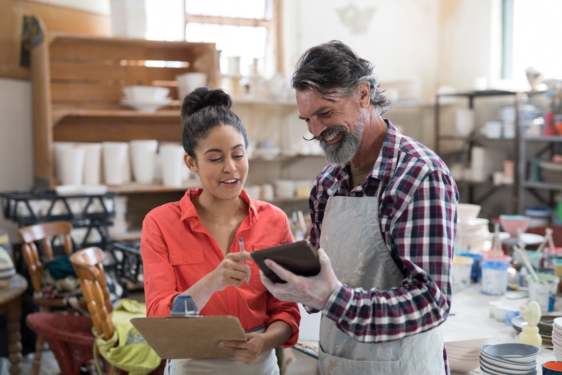 A man and a woman are looking at a tablet in a pottery shop.