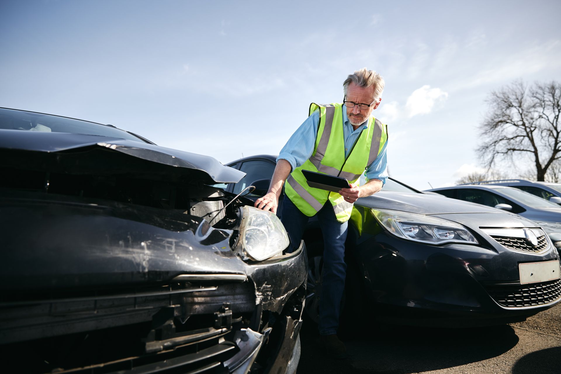 A man in a yellow vest is standing next to a damaged car.