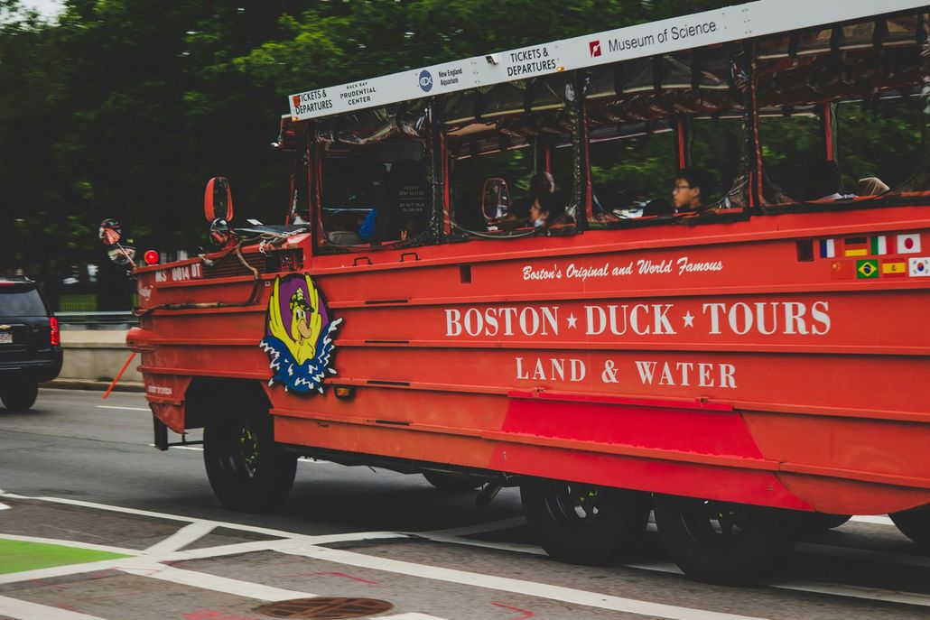 A red boston duck tours bus is parked on the side of the road.