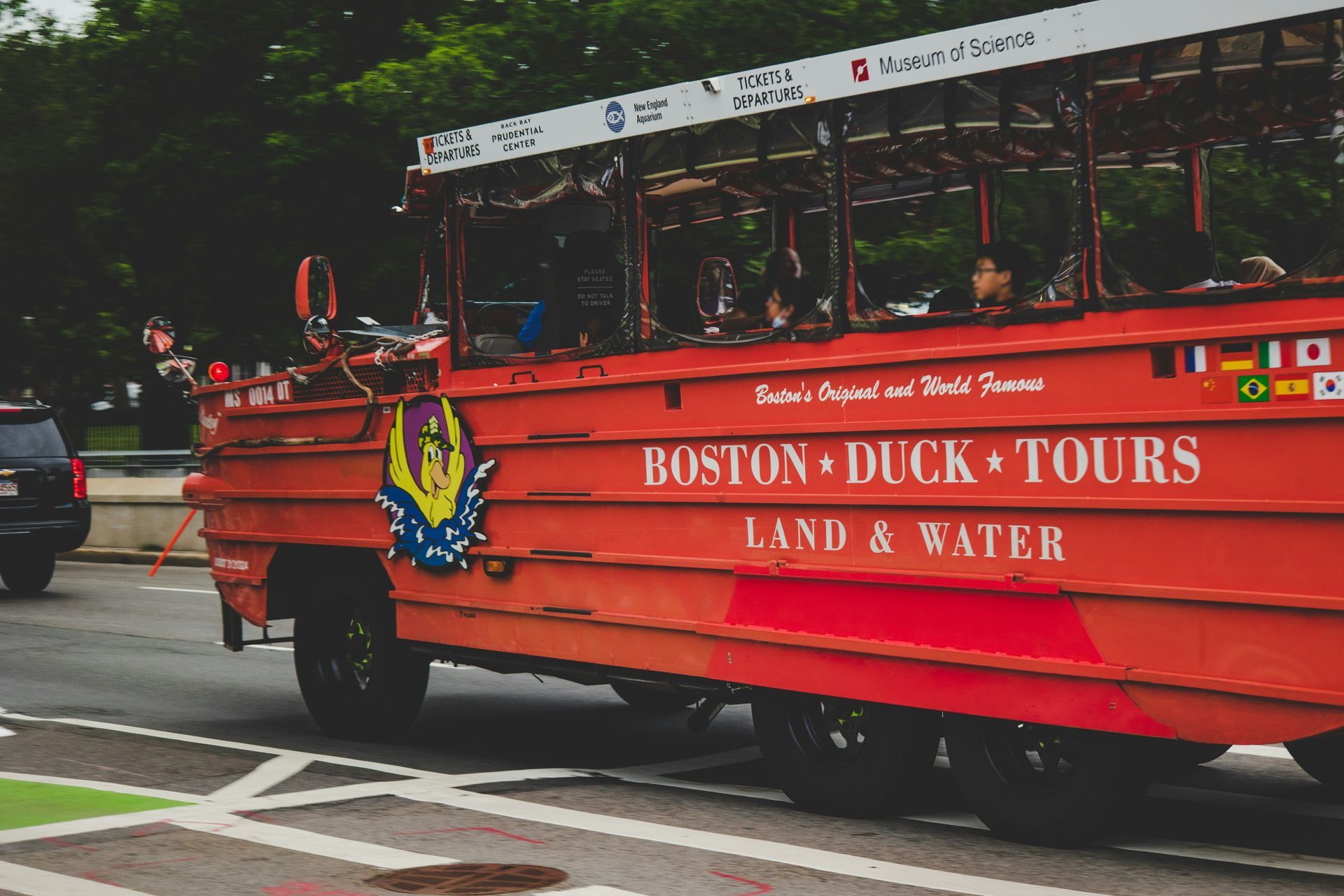 A red boston duck tours bus is parked on the side of the road.