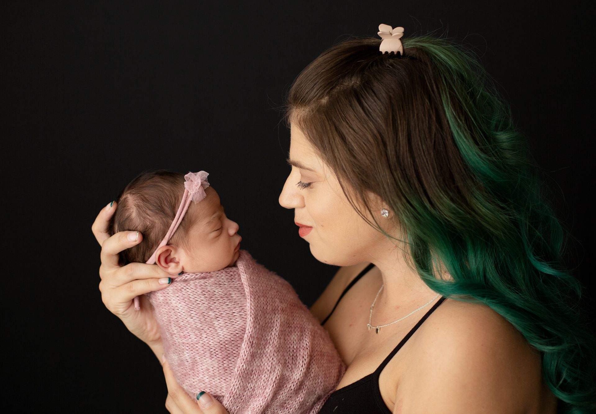 A woman with green hair is holding a newborn baby wrapped in a pink blanket.