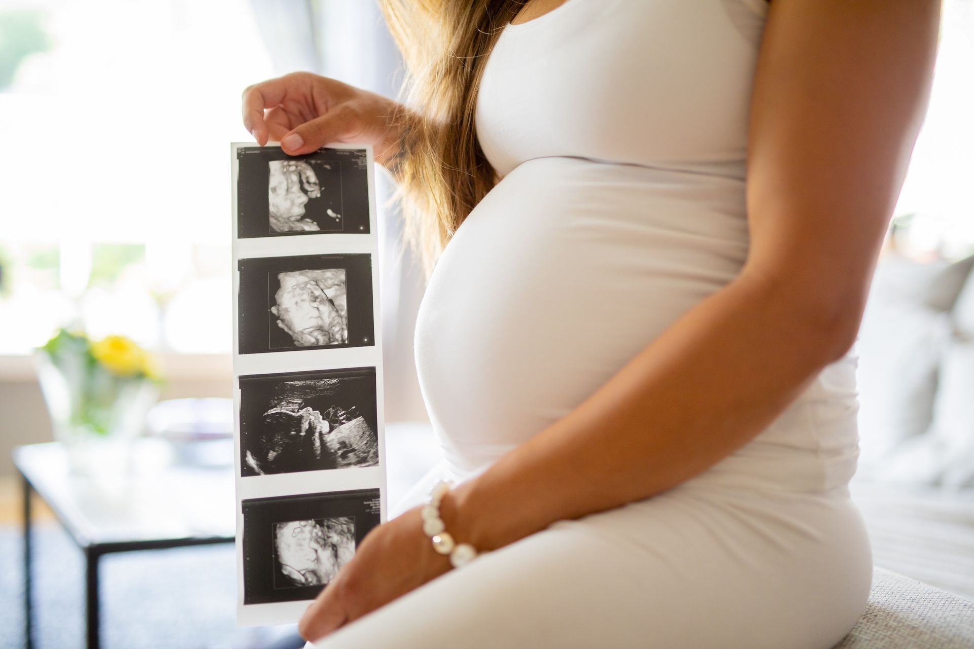 A pregnant woman is holding a stack of ultrasound images.