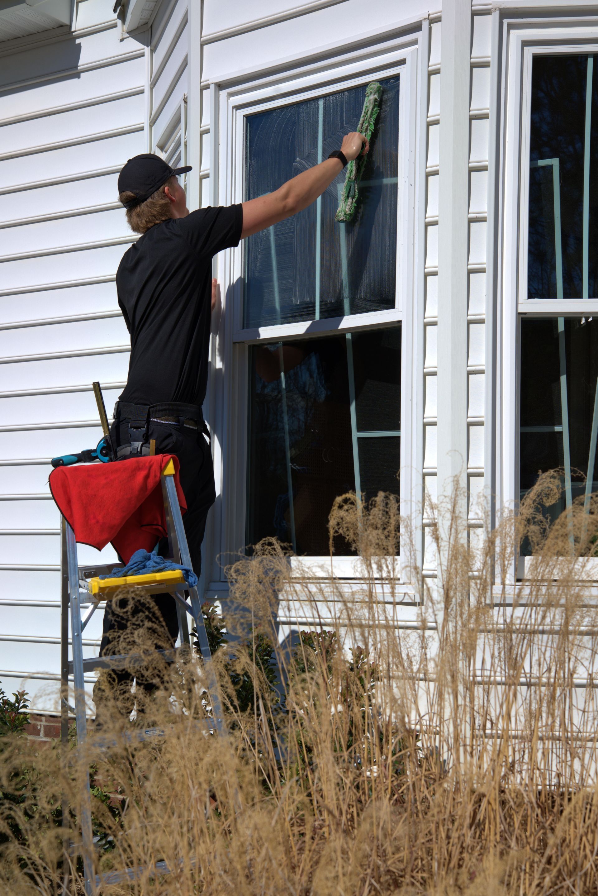 Window cleaner washing window on a house using a squeegee. He is on a ladder.