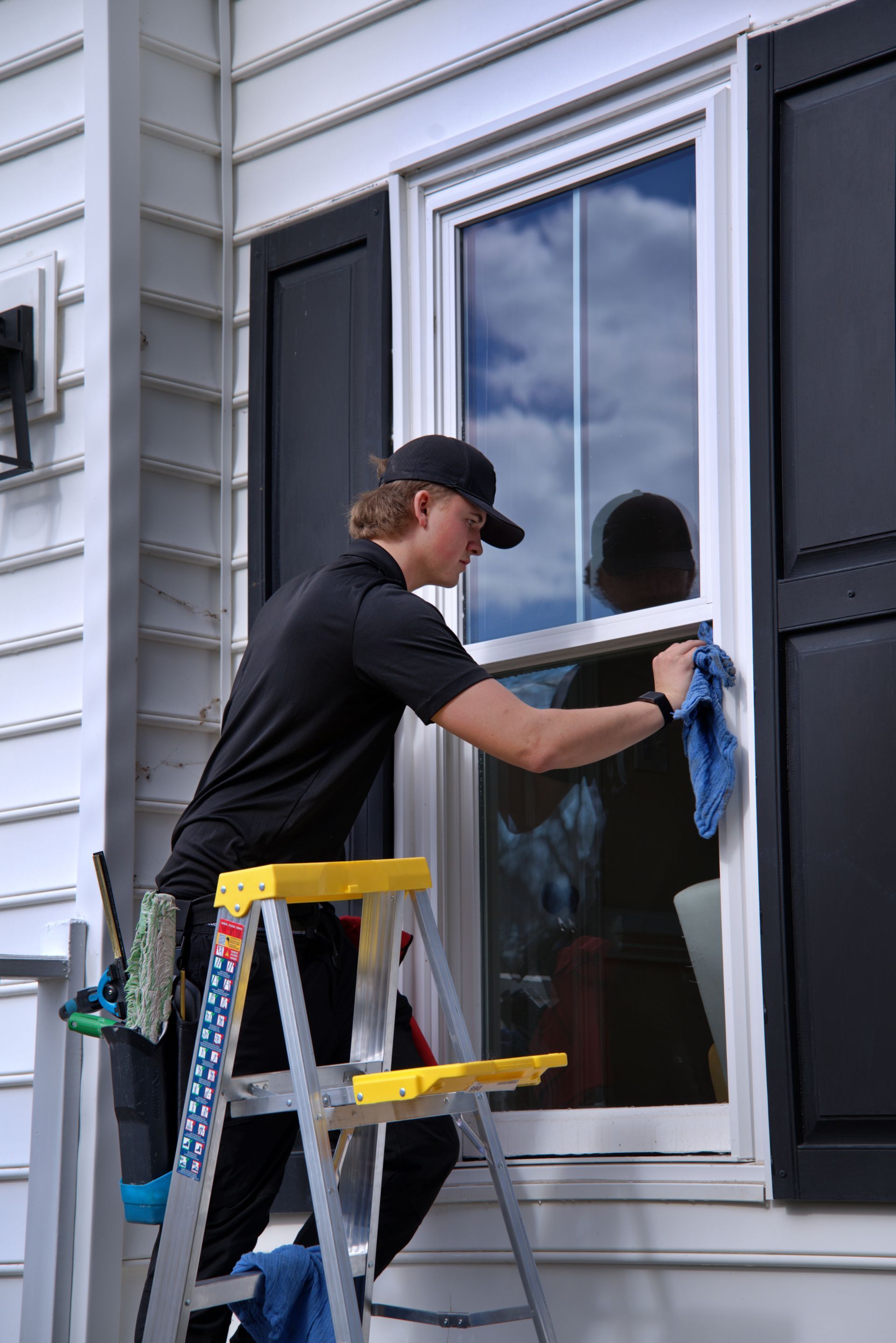 Person wearing yellow glove using a squeegee to clean a window with soapy water.