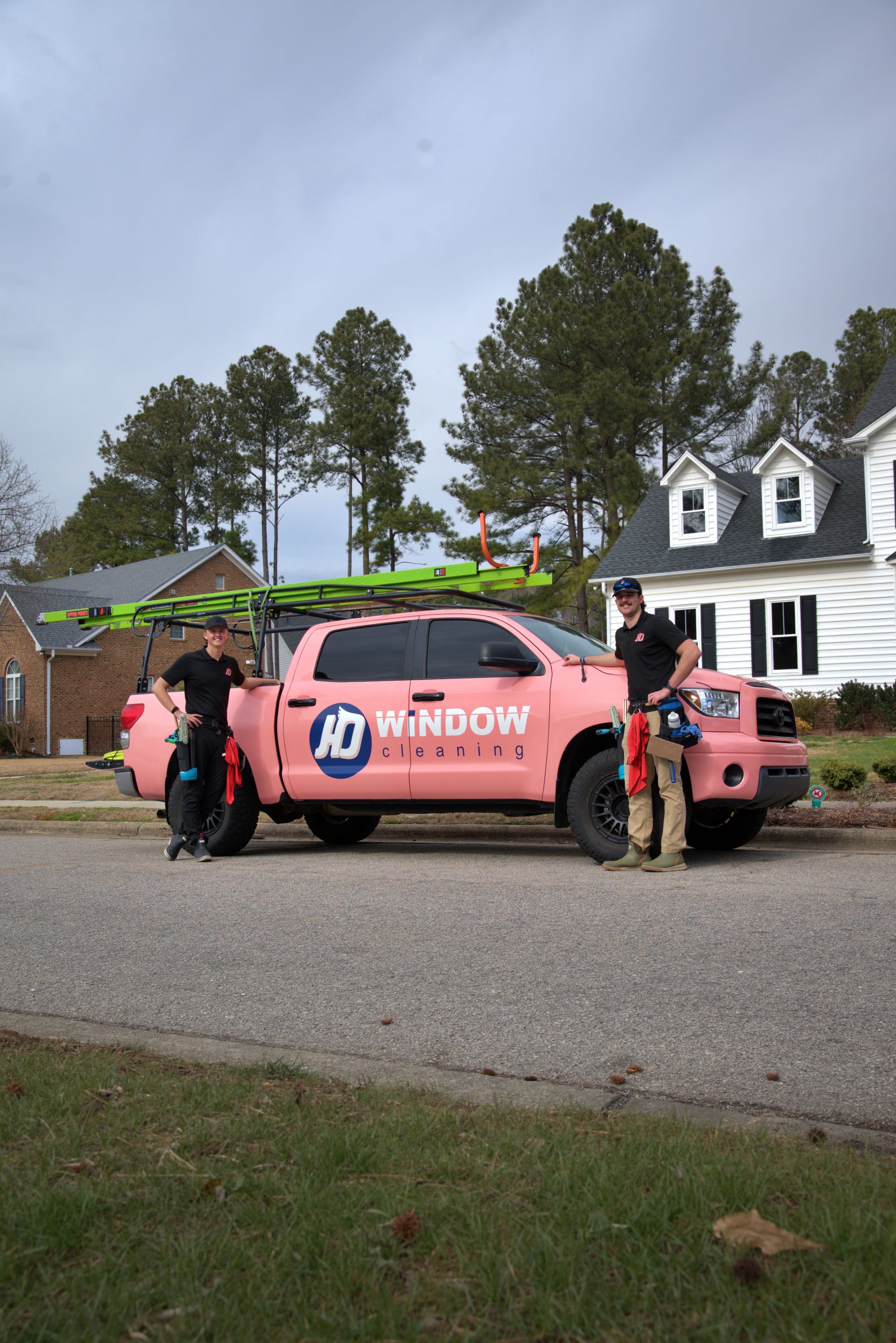 Two men beside a pink truck with window cleaning equipment. The truck has the 