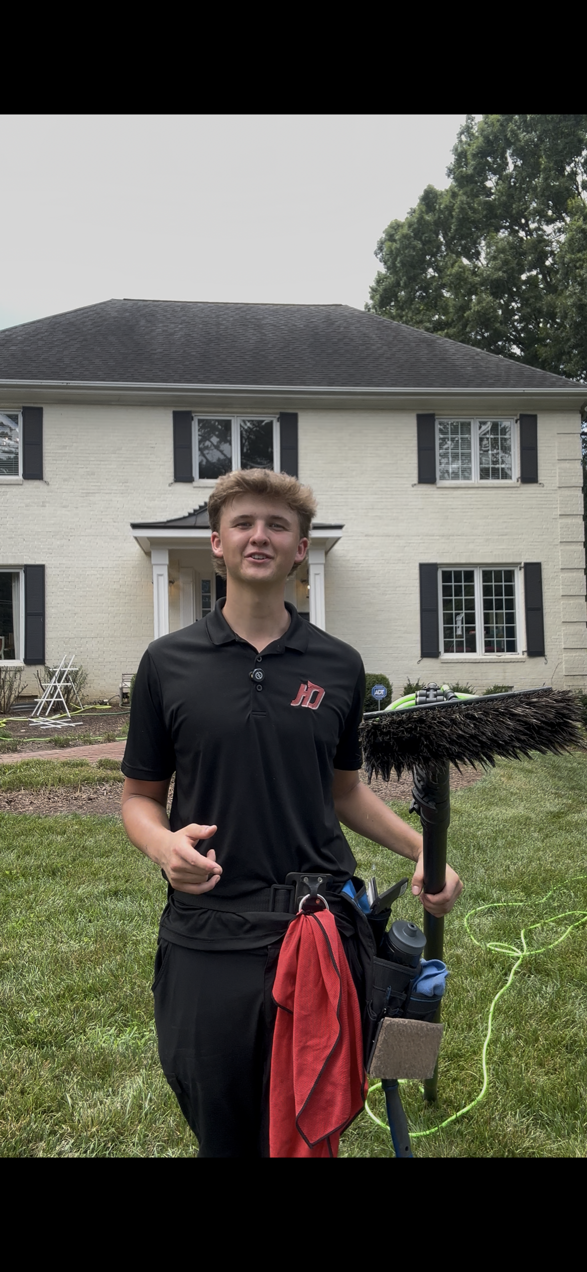 A person in black shirt and pants holding cleaning equipment stands in front of a house.