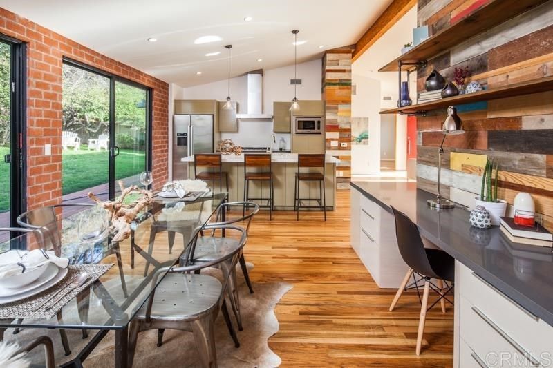 A dining room with a glass table and chairs and a kitchen with sliding glass doors.