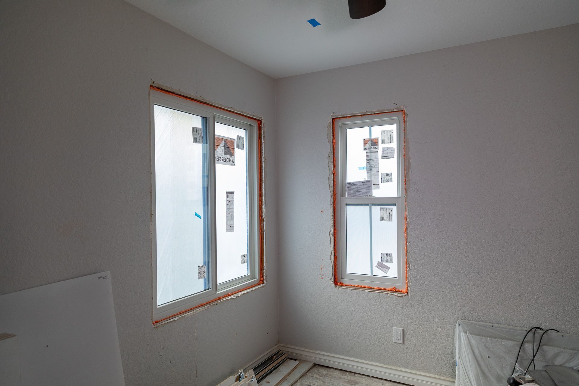 An empty room with two windows and a ceiling fan.