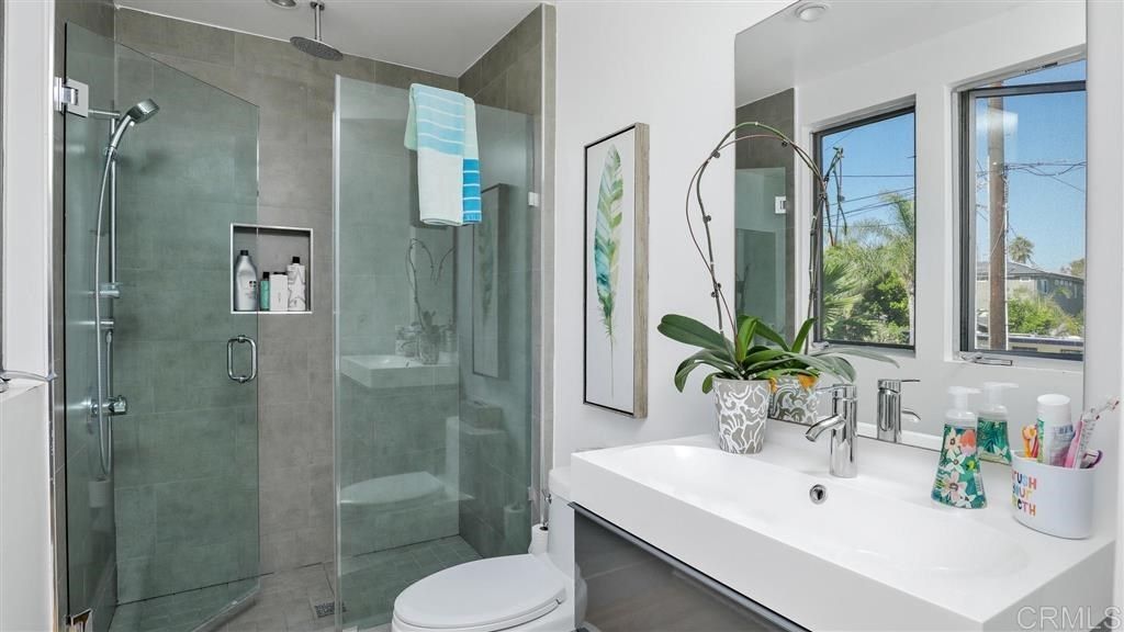 A bathroom with a toilet, sink, shower and mirror.