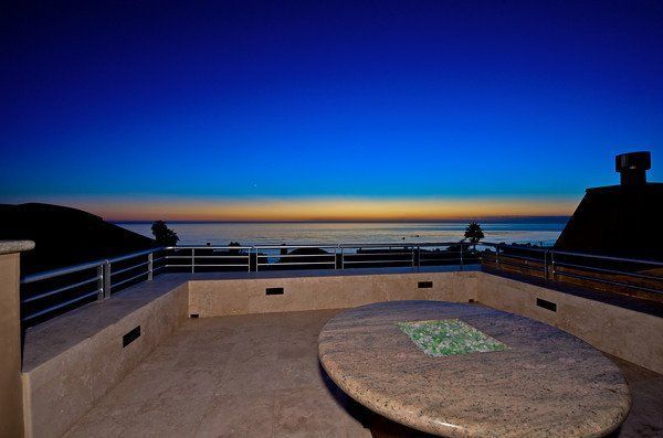 A balcony with a table and a view of the ocean at sunset.