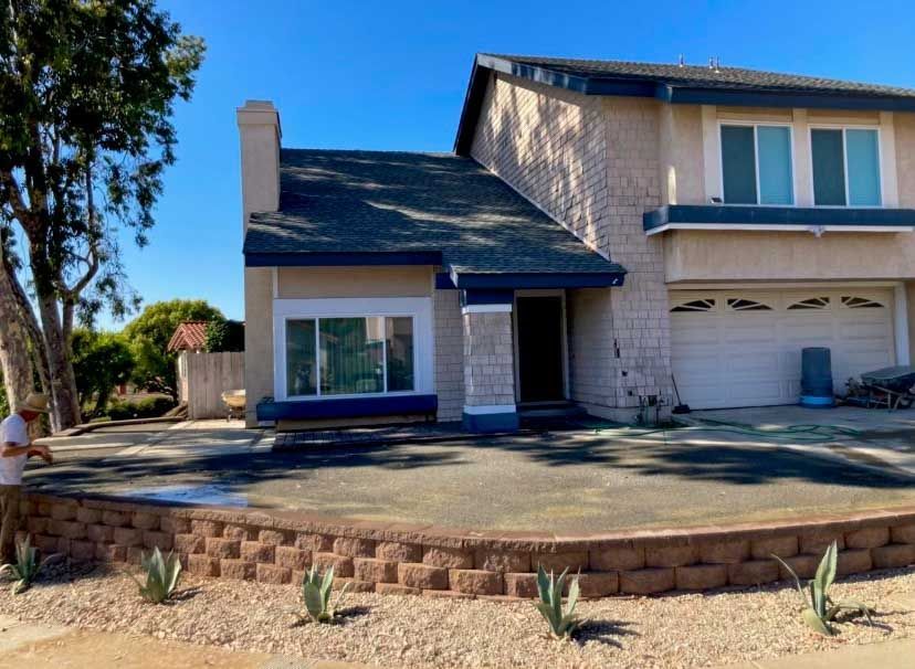 A man is sitting in front of a large house, under remodel construction.