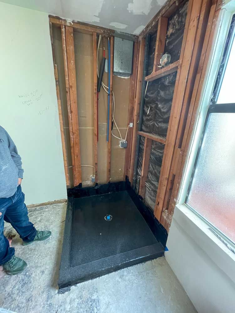 A man is standing in a room with a shower stall under construction.