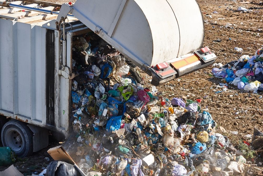 A garbage truck is dumping a pile of trash into the ground.