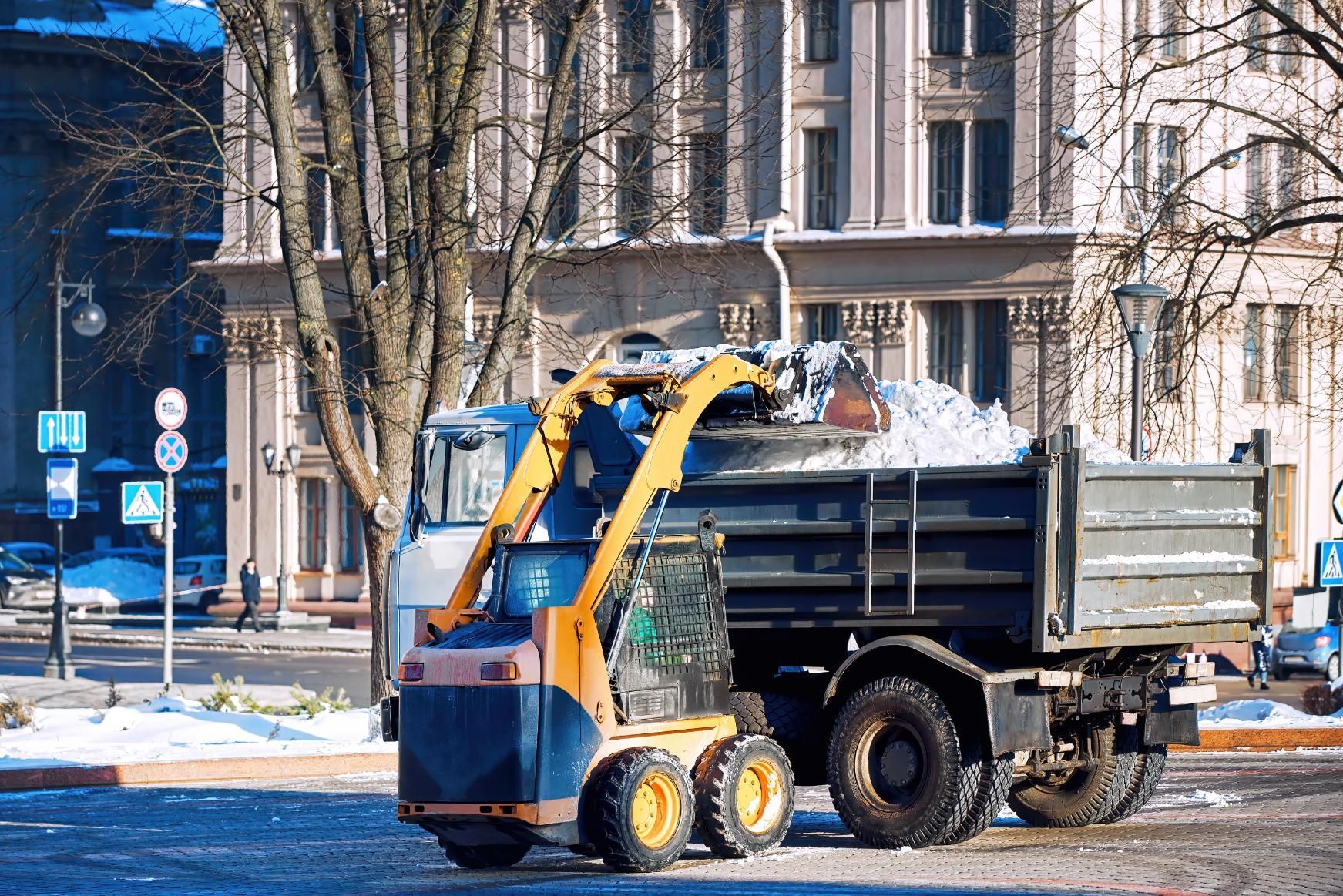 A snow plow is loading snow into a dump truck.