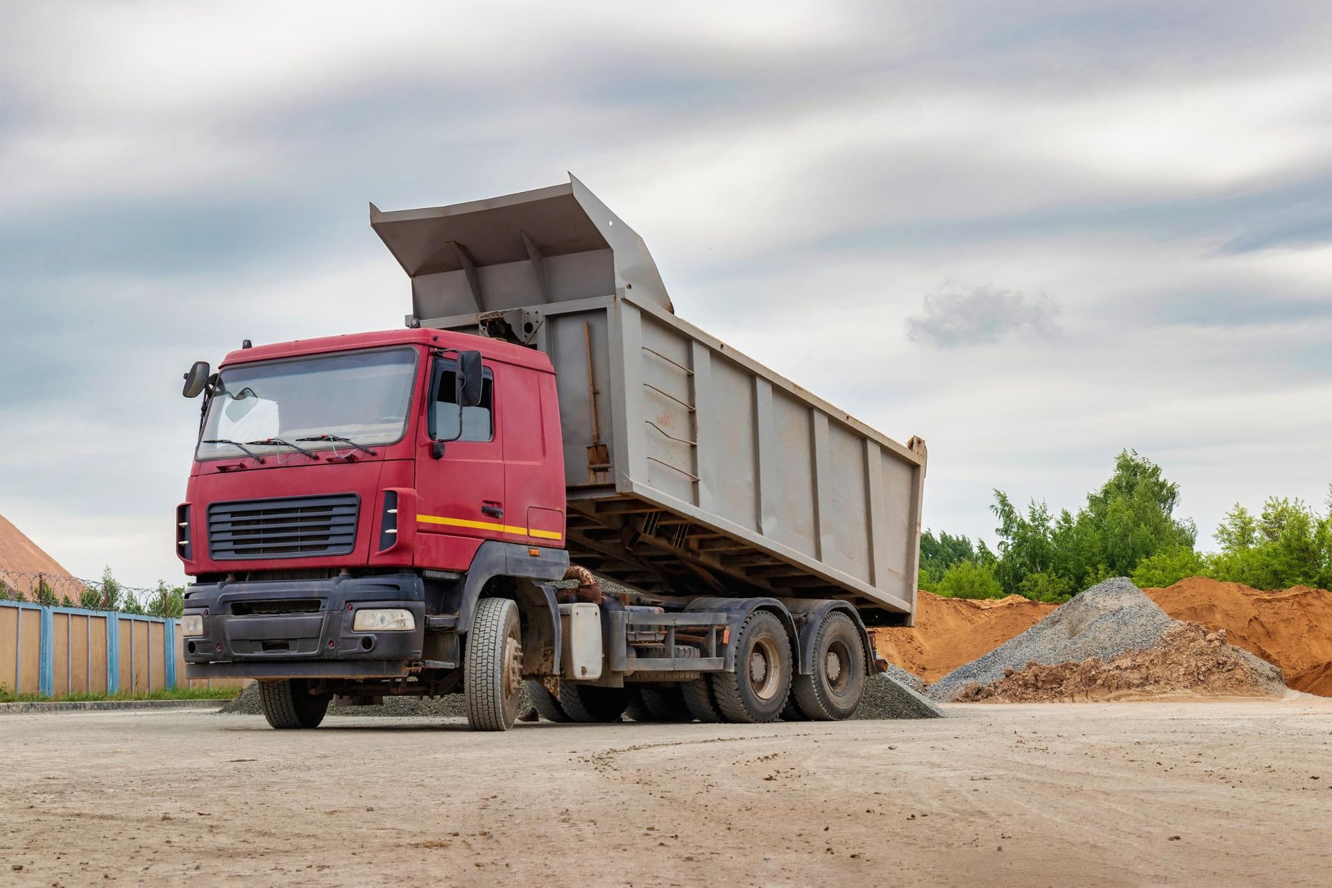 A red dump truck is driving down a dirt road.