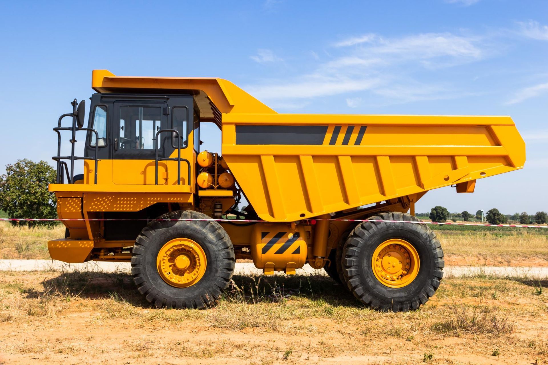 A large yellow dump truck is parked in a field.