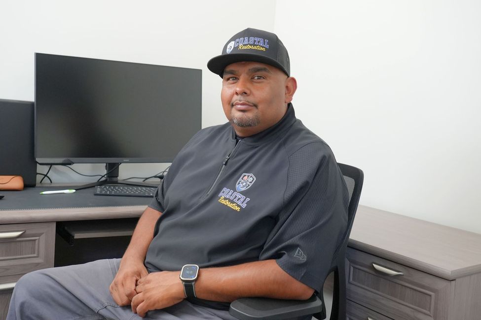 Man in black CRS shirt and cap talking on a phone at a desk
