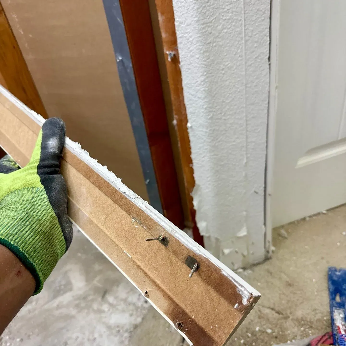 Gloved hand holding a wooden door frame panel with nails near a doorway and wall corner