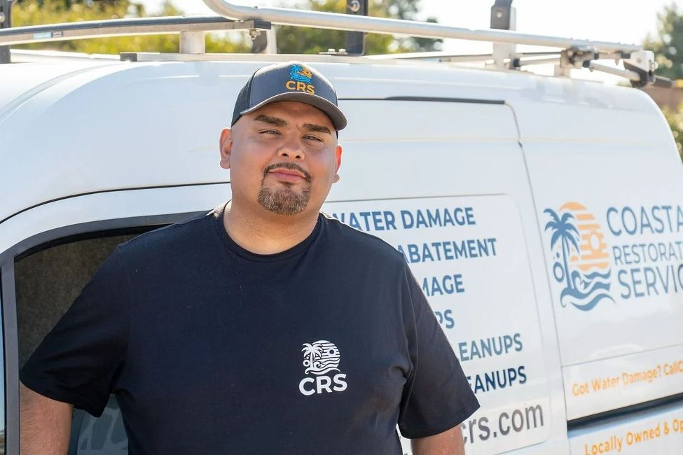 Man standing beside a white Coastal Restoration Services van with water damage cleanup text