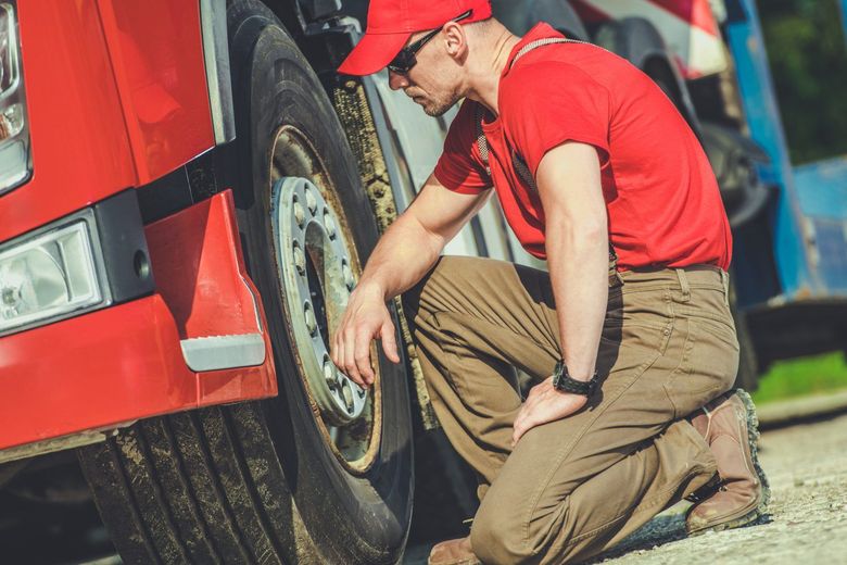 Man in red shirt and cap inspecting the tire of a red truck.