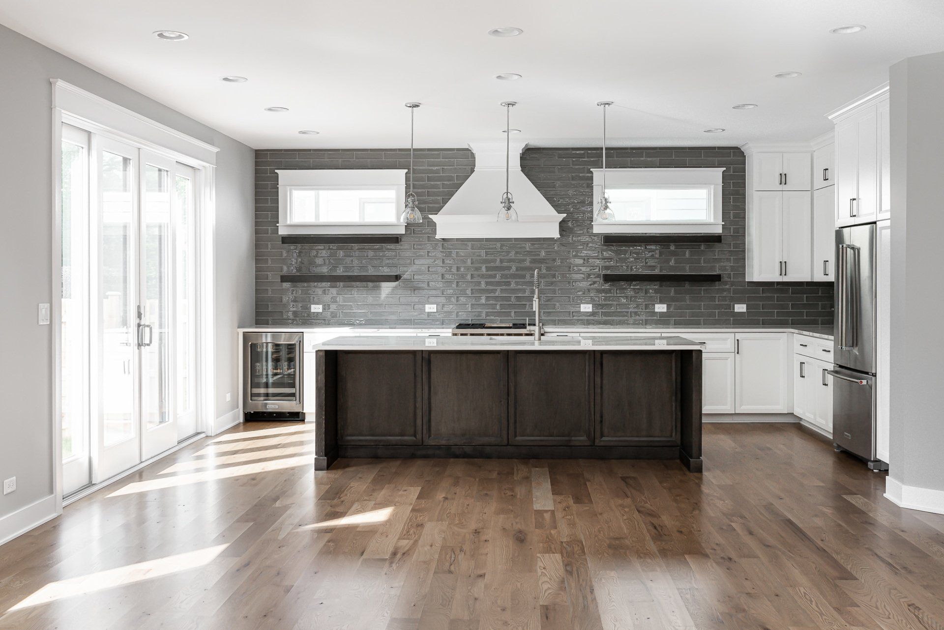 An empty kitchen with hardwood floors , white cabinets , stainless steel appliances and a large island.