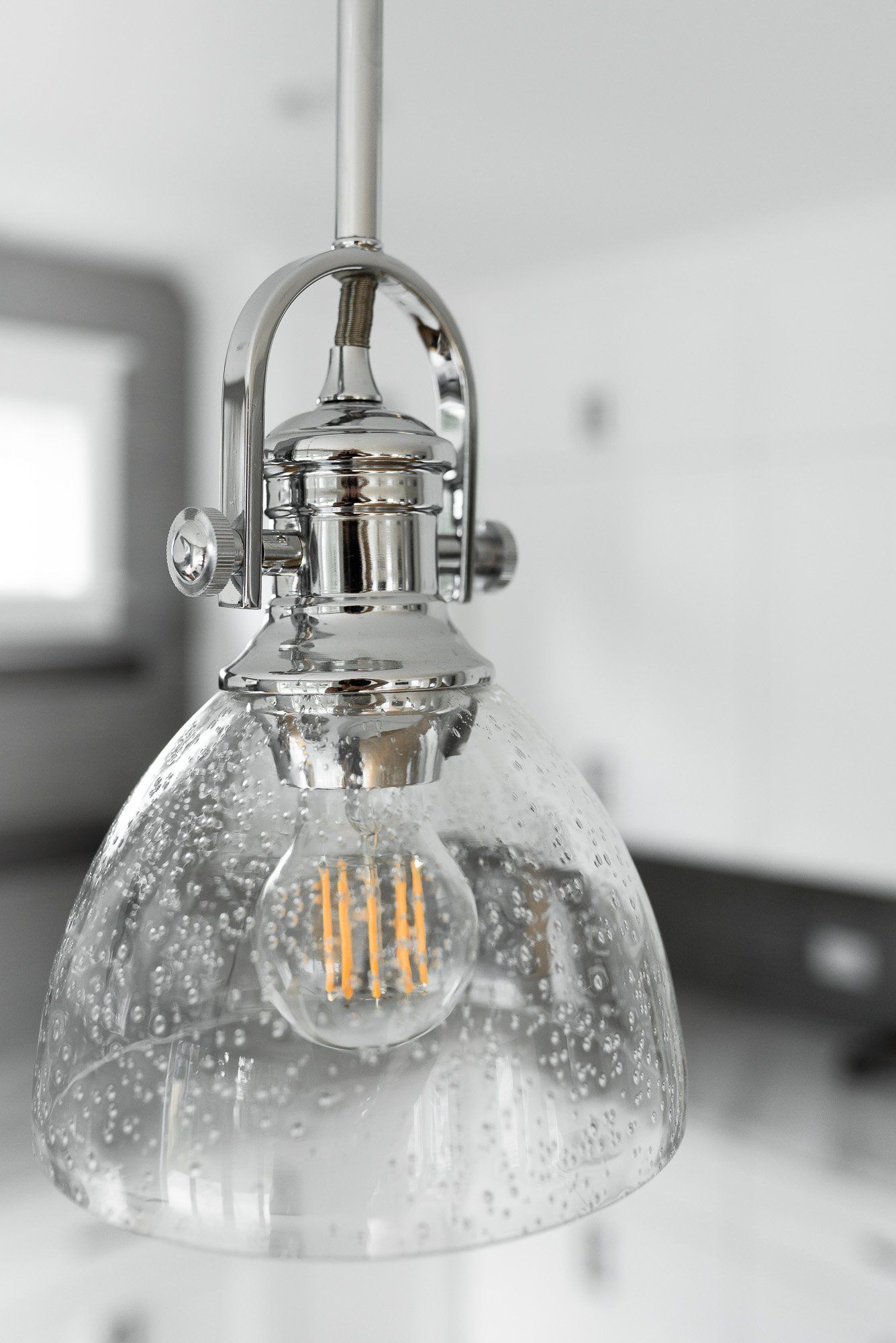 A pendant light with a clear glass shade is hanging from the ceiling in a kitchen.