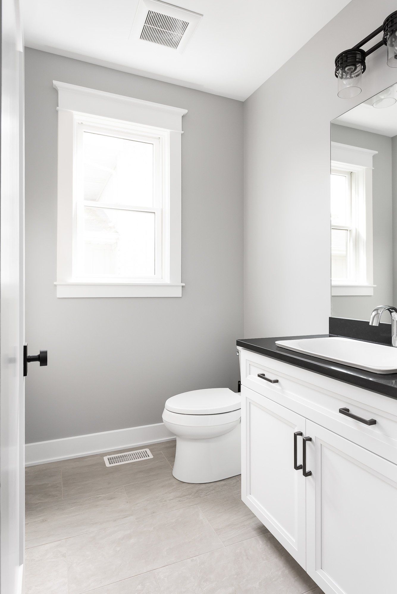 A bathroom with a toilet , sink , mirror and window.