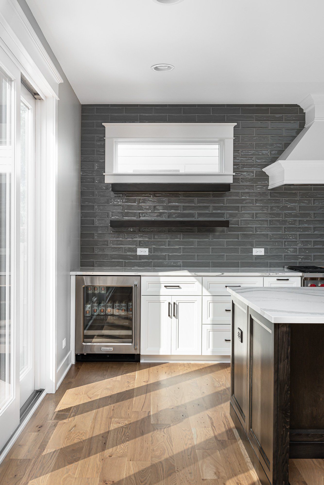 A kitchen with white cabinets , a stainless steel refrigerator , and a brick wall.