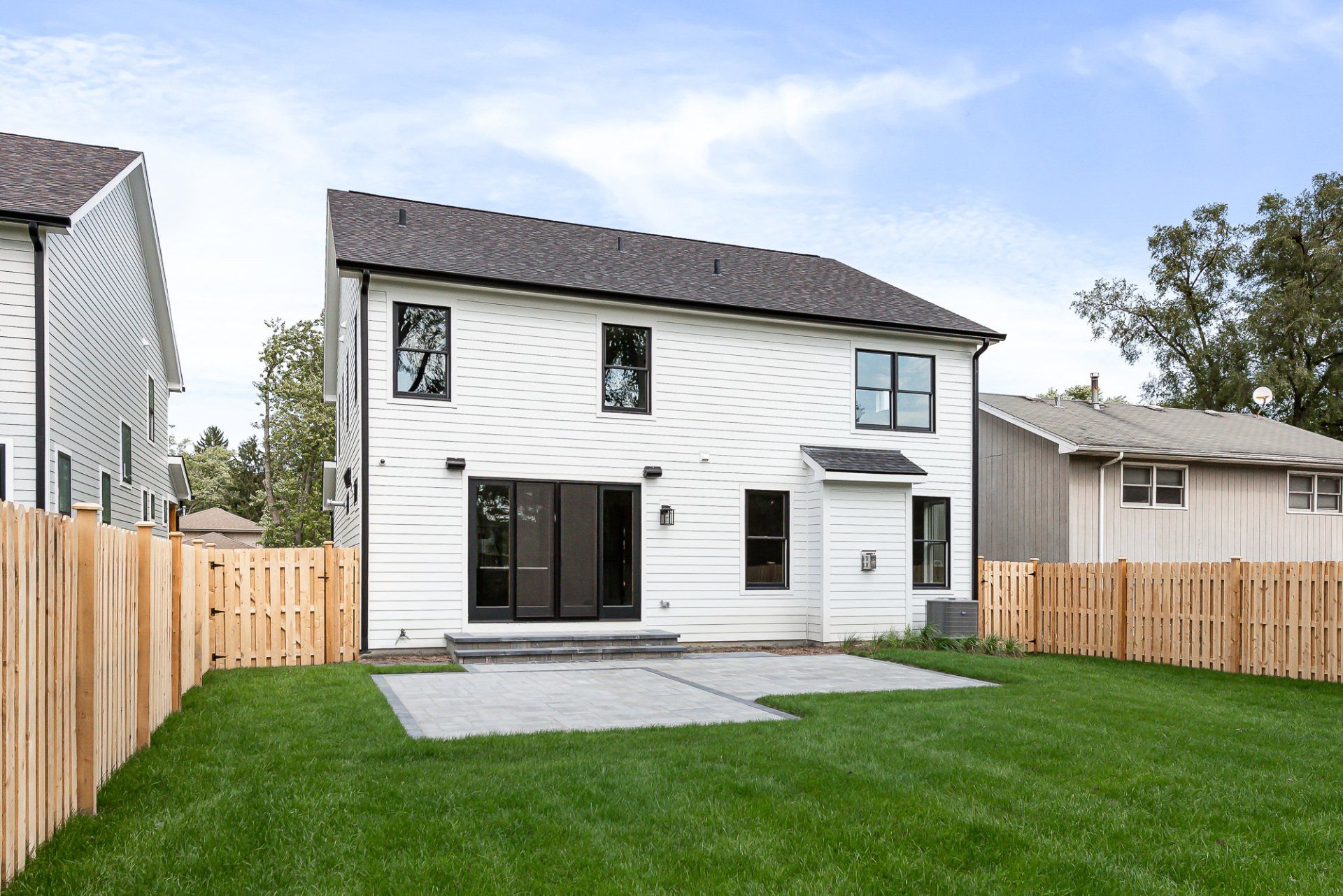 The backyard of a white house with a wooden fence
