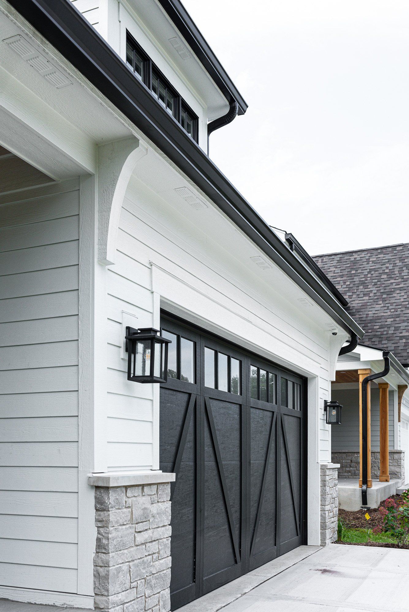 A black garage door is on the side of a white house.