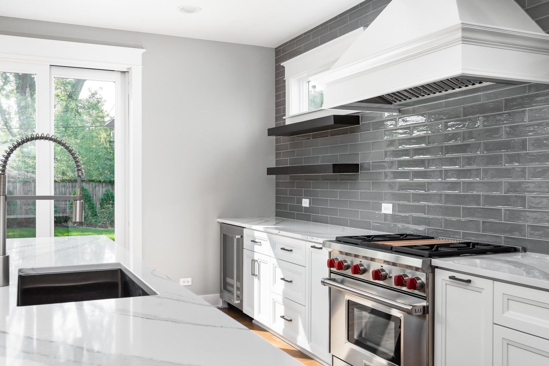 A kitchen with white cabinets , a stove , a sink , and a window.