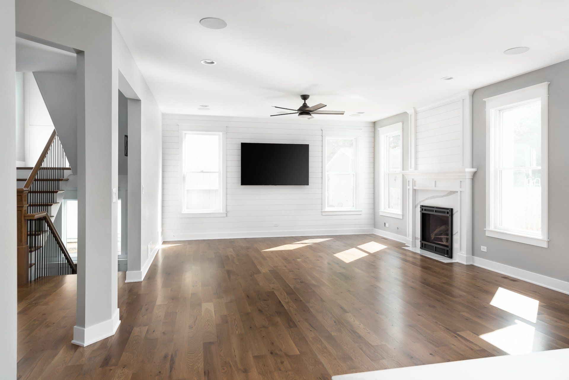 An empty living room with hardwood floors , a fireplace , a flat screen tv and a ceiling fan.