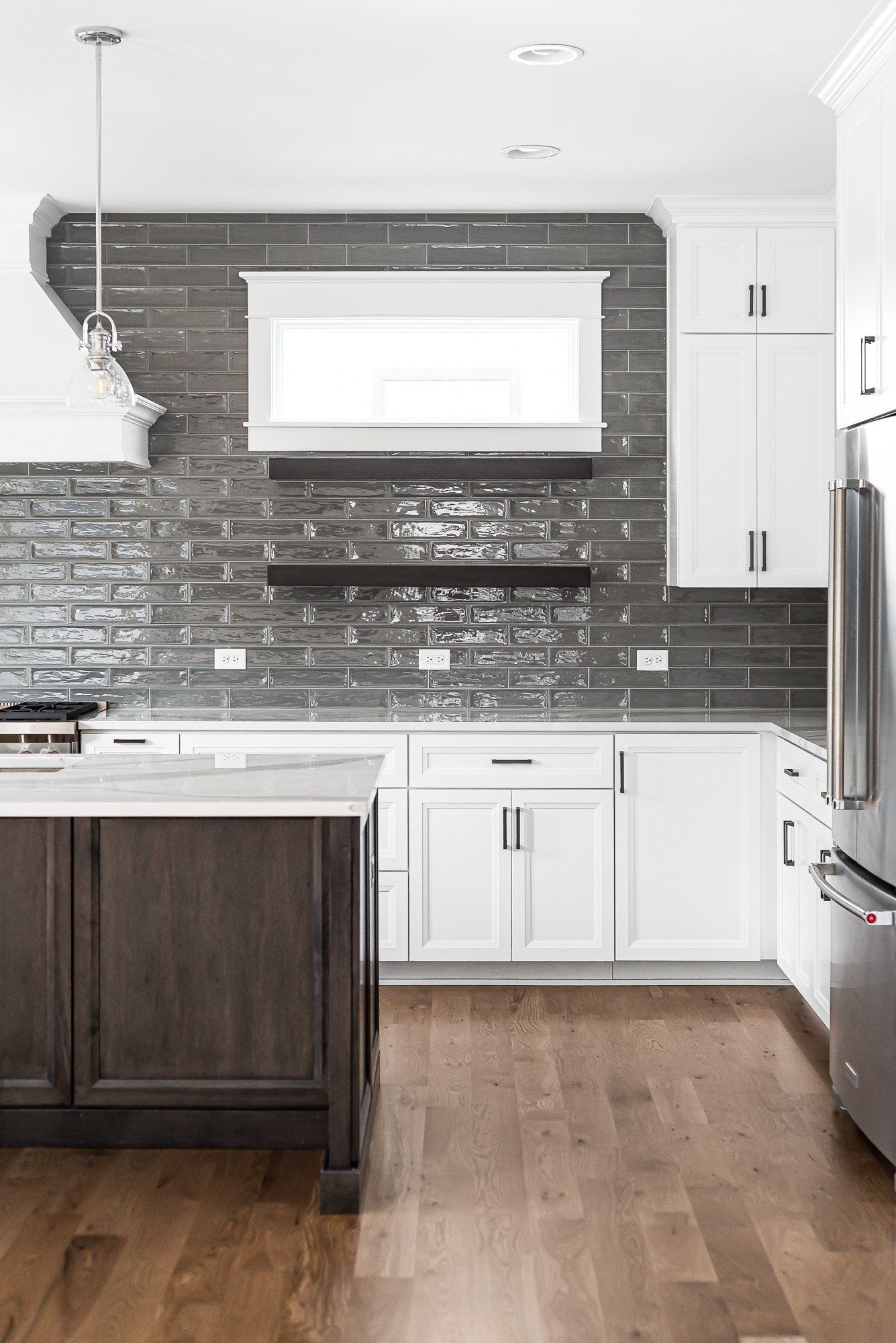 A kitchen with white cabinets , wooden floors , stainless steel appliances and a brick wall.