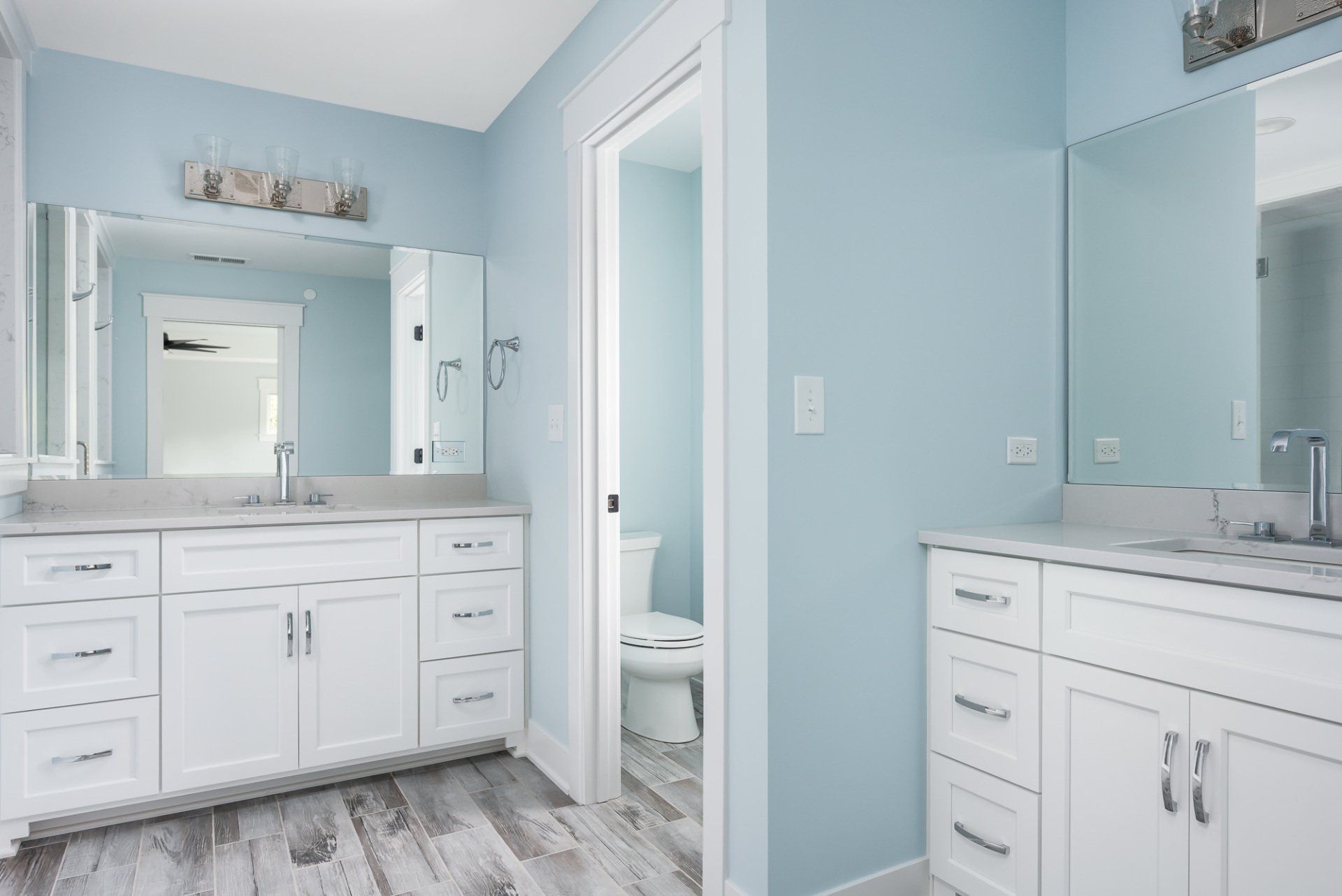 A bathroom with two sinks , two mirrors and a toilet.