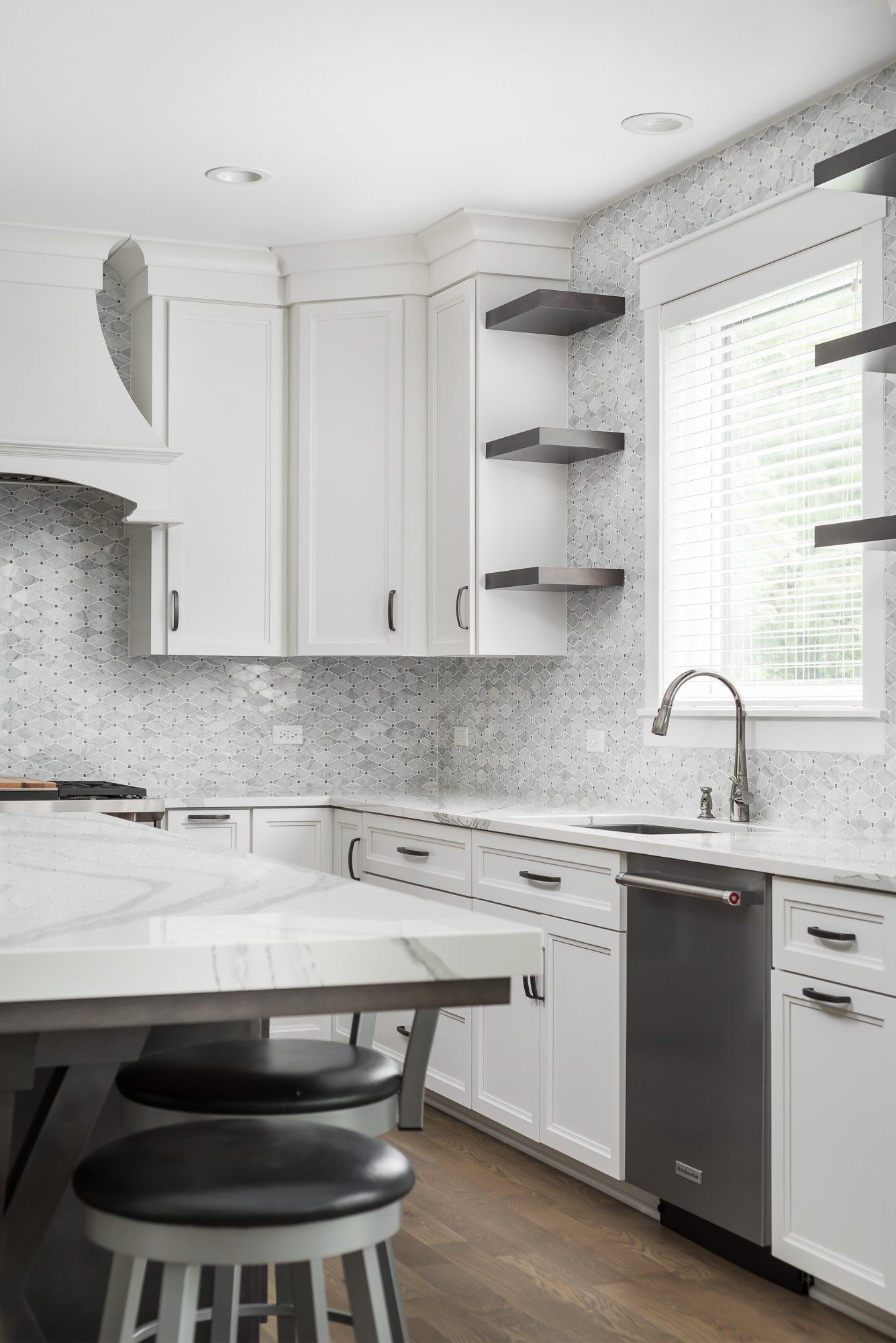 A kitchen with white cabinets , black stools , a sink , and a window.