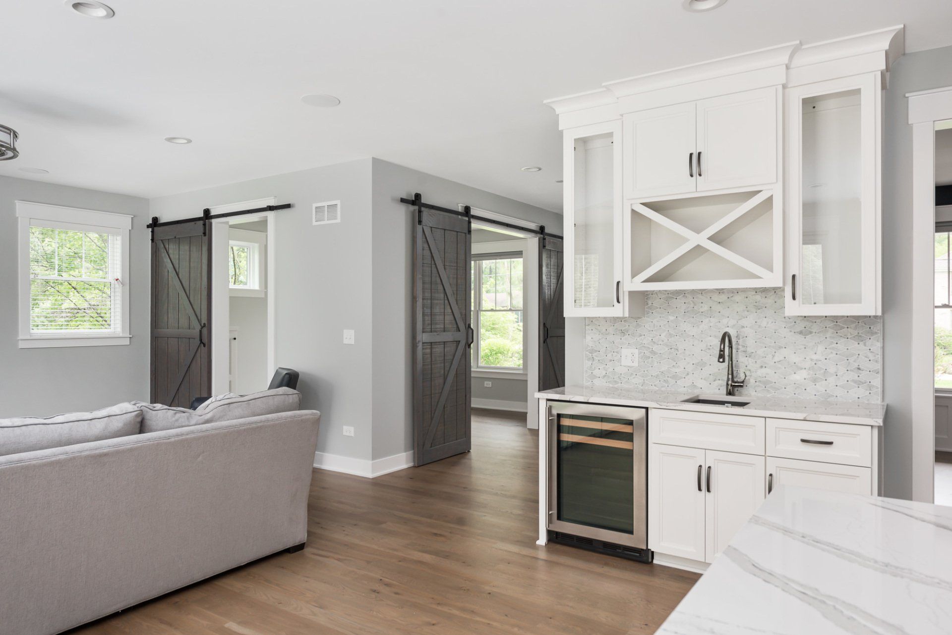 A kitchen with white cabinets and sliding barn doors leading to a living room.