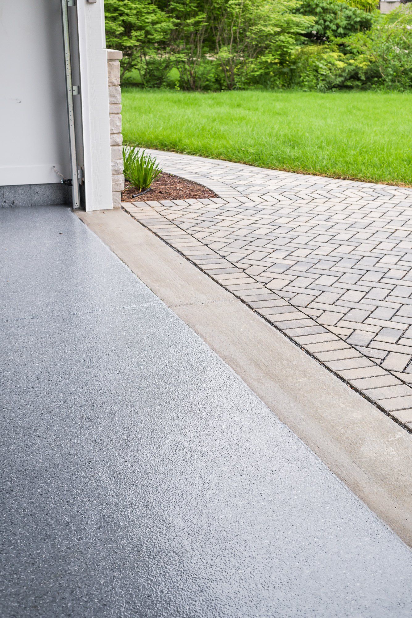 A garage with a gray floor and a brick driveway leading to a lush green yard.