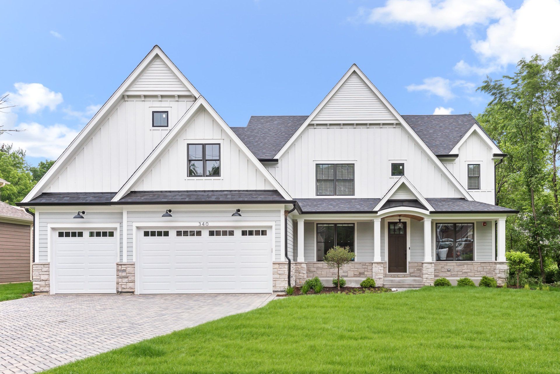 A large white house with a gray roof and two garage doors is sitting on top of a lush green lawn.