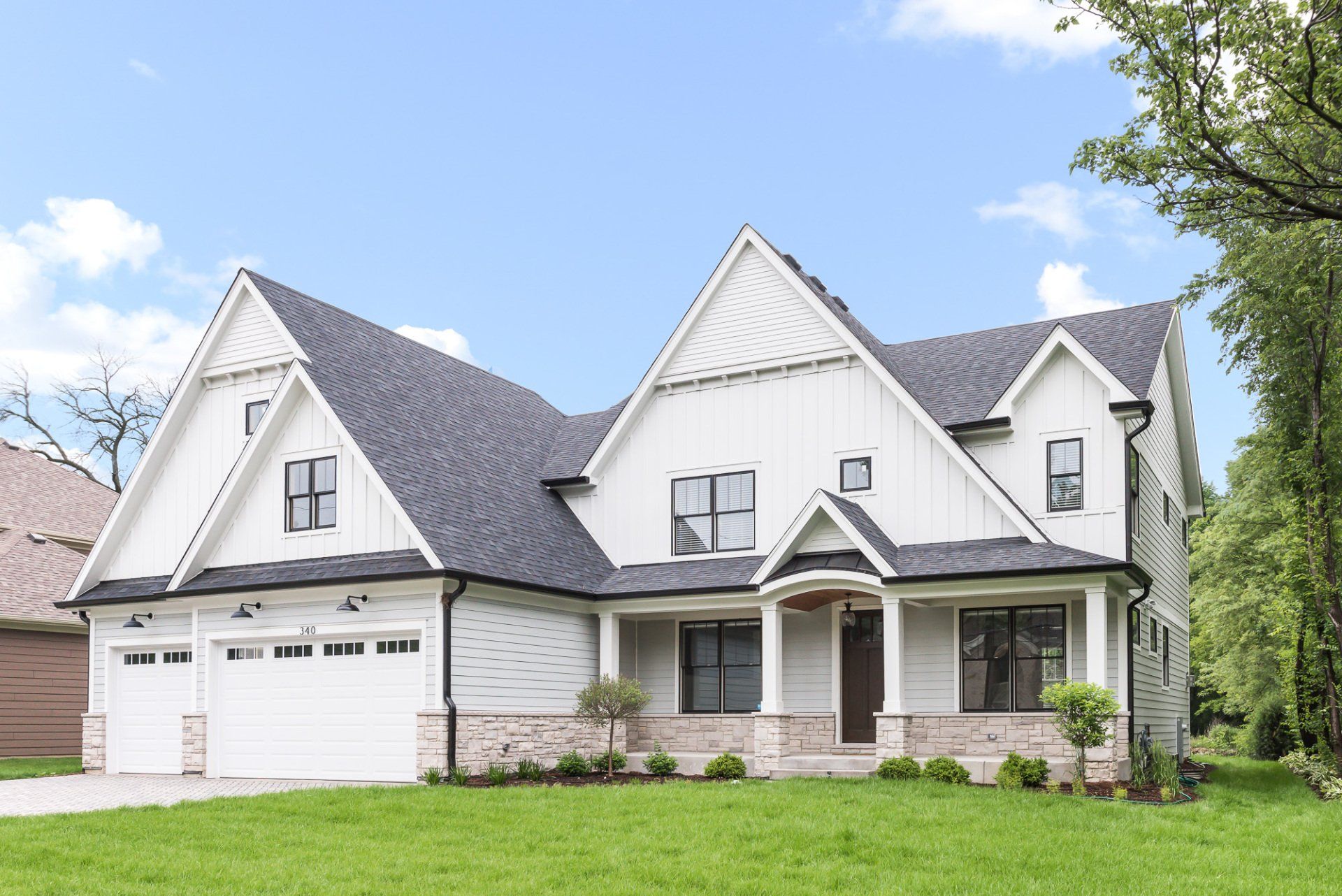 A large white house with a black roof is sitting on top of a lush green lawn.