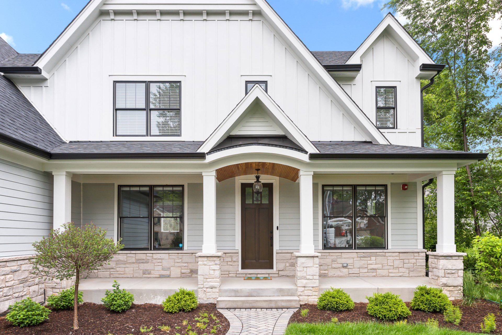 A white house with a large porch and a black roof.