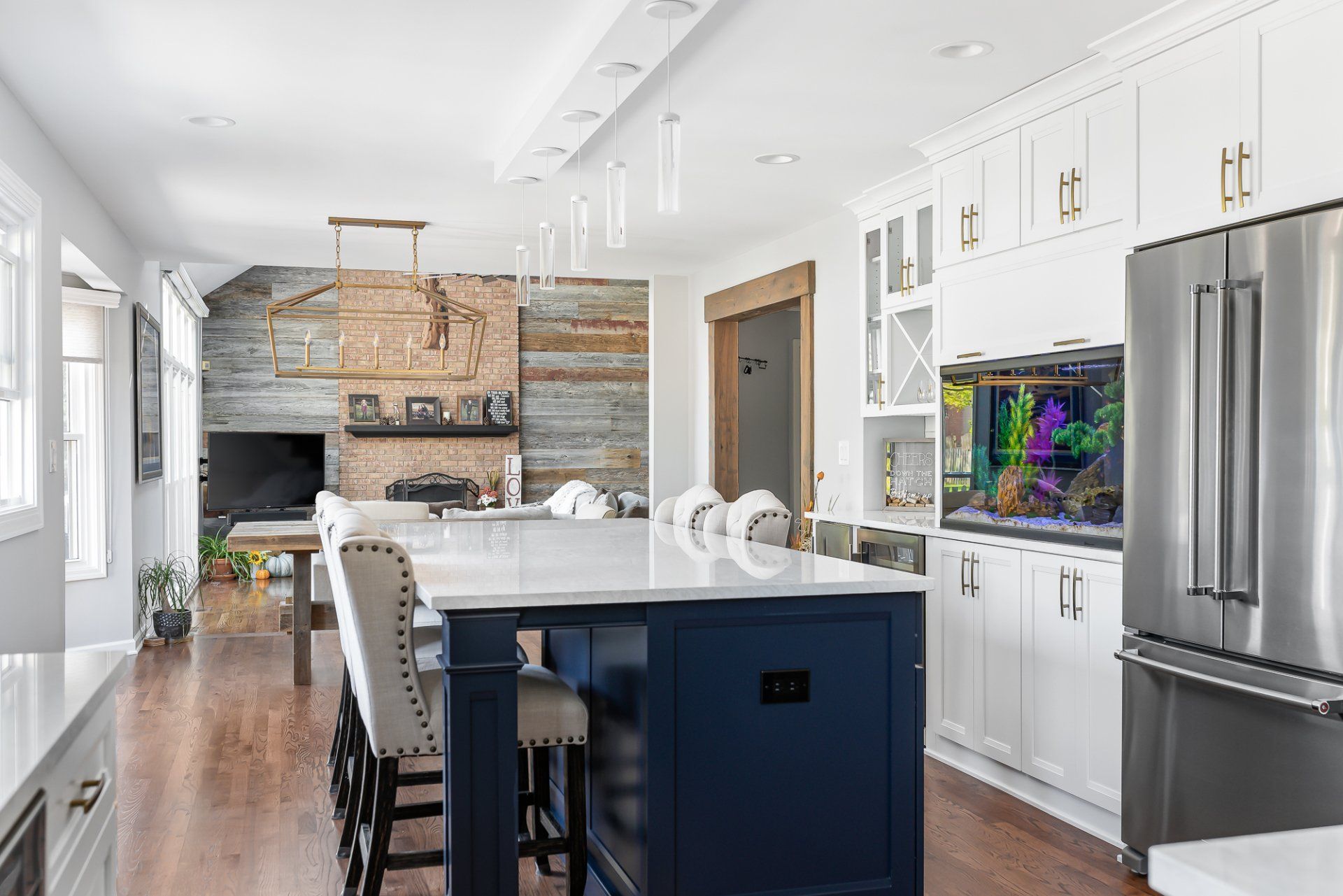 A kitchen with a blue island , white cabinets , stainless steel appliances and a fish tank.