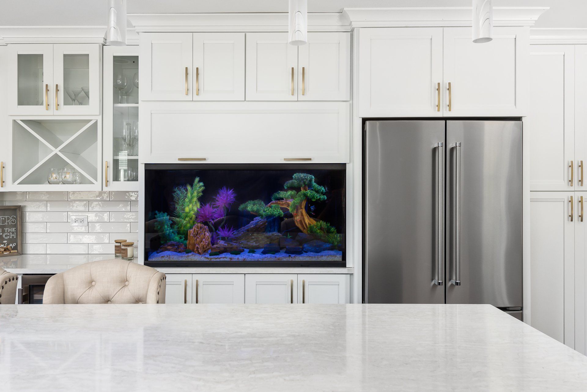 A kitchen with white cabinets , a stainless steel refrigerator , and an aquarium.