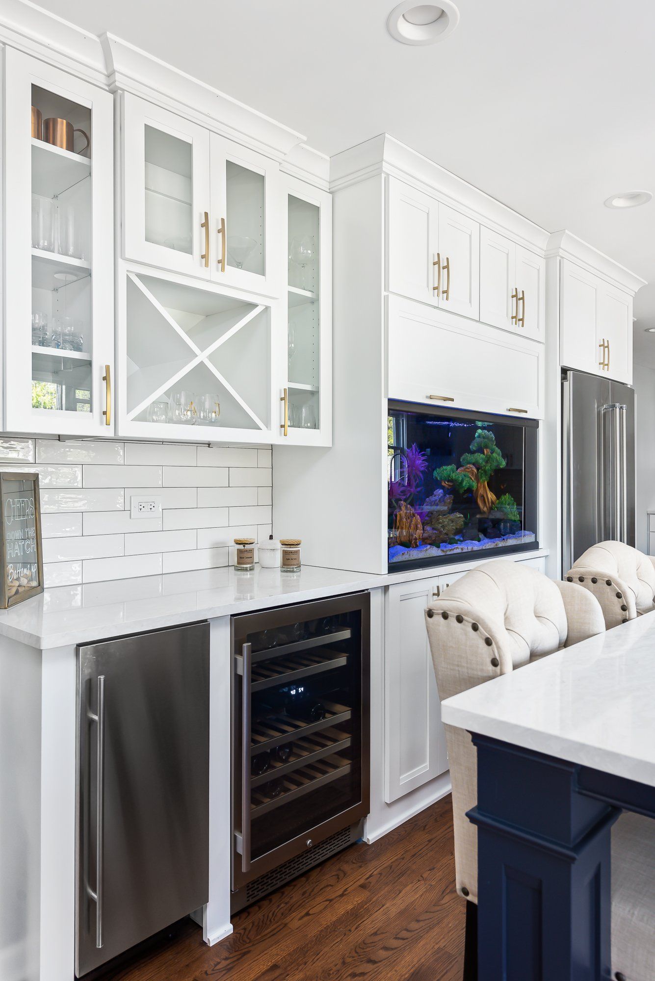 A kitchen with white cabinets , stainless steel appliances , a wine cooler and a fish tank.