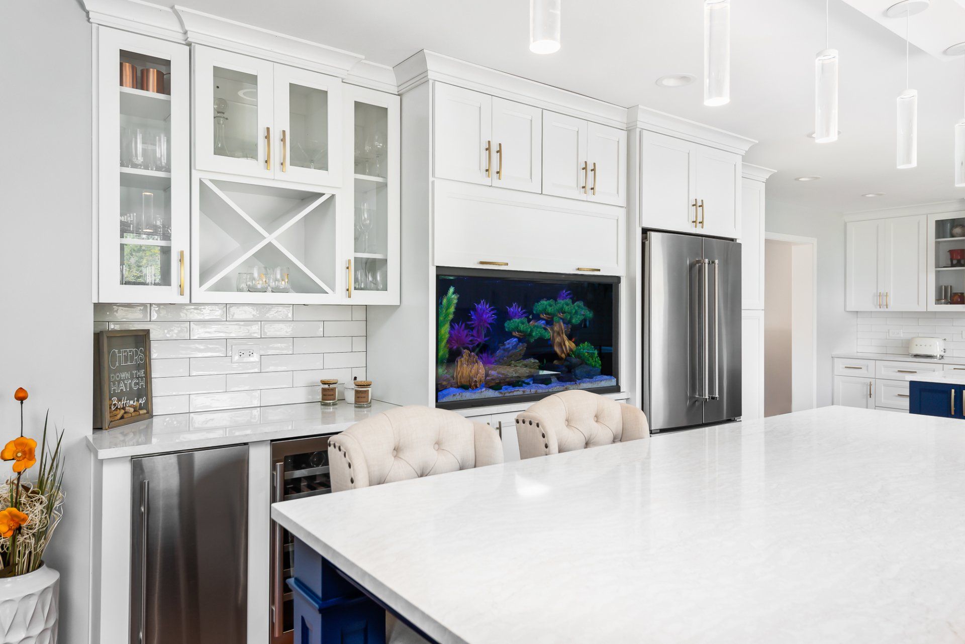 A kitchen with white cabinets , stainless steel appliances , a large island and an aquarium.