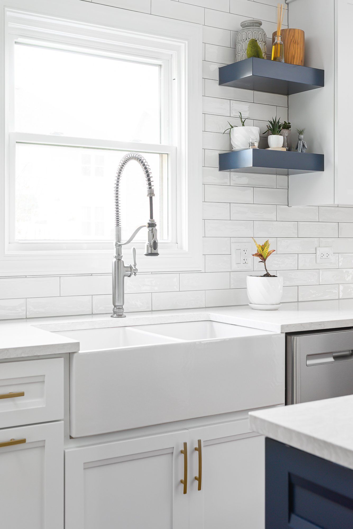 A kitchen with a white sink , white cabinets , and a window.