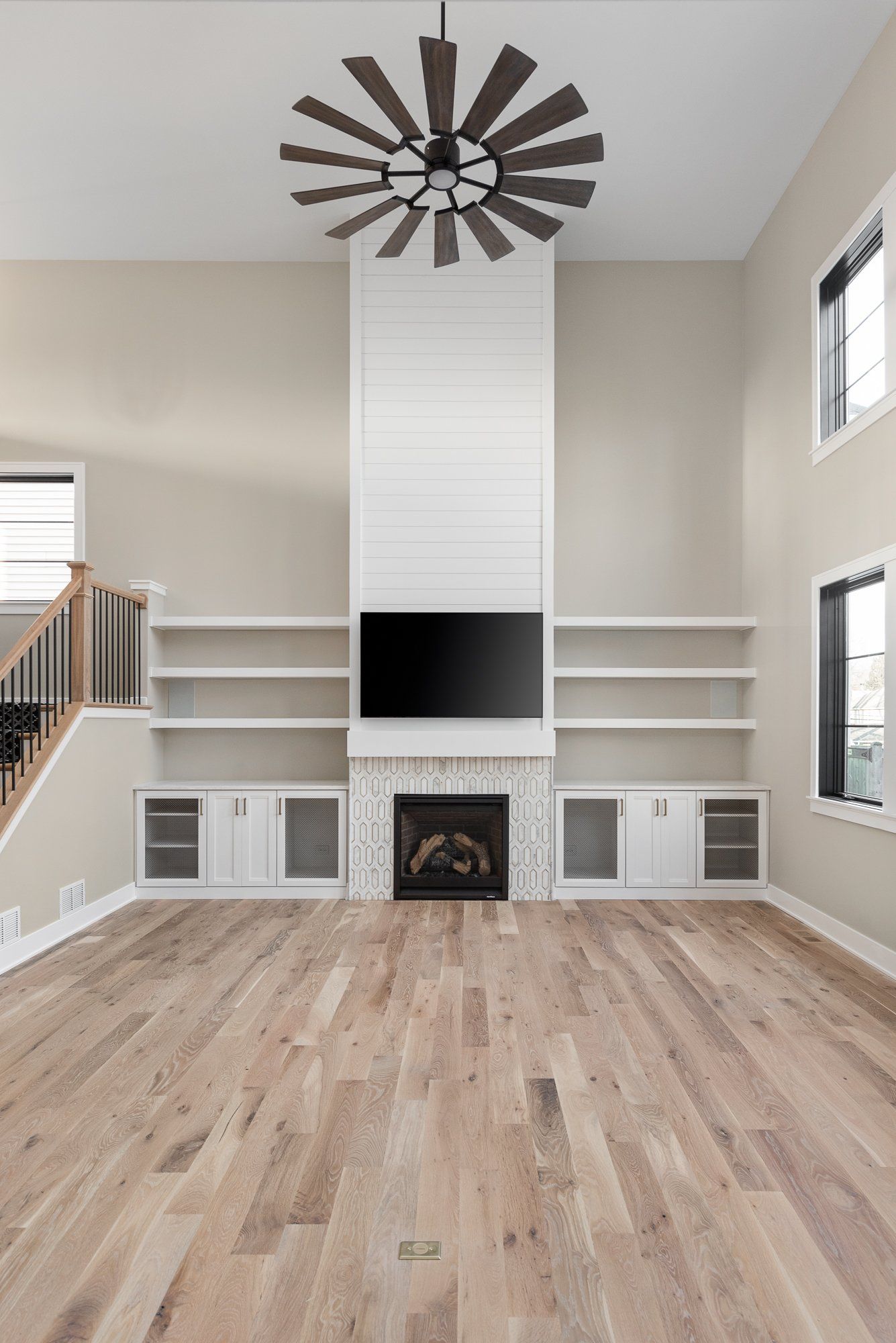 A living room with hardwood floors , a fireplace , a flat screen tv and a ceiling fan.