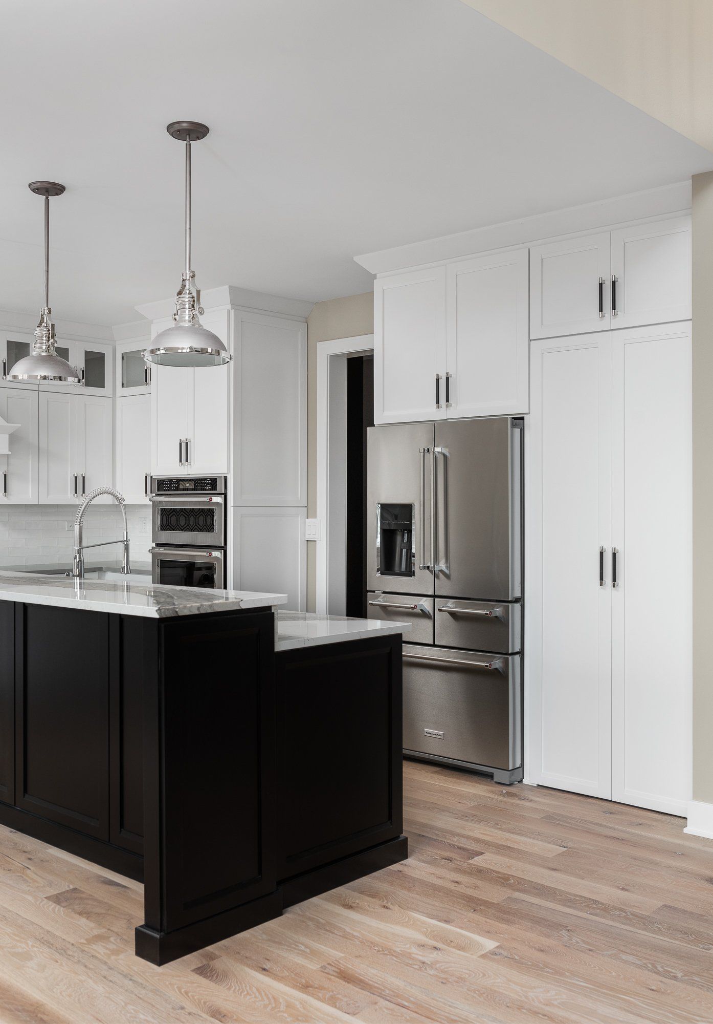 A kitchen with a black island , white cabinets , stainless steel appliances , and hardwood floors.